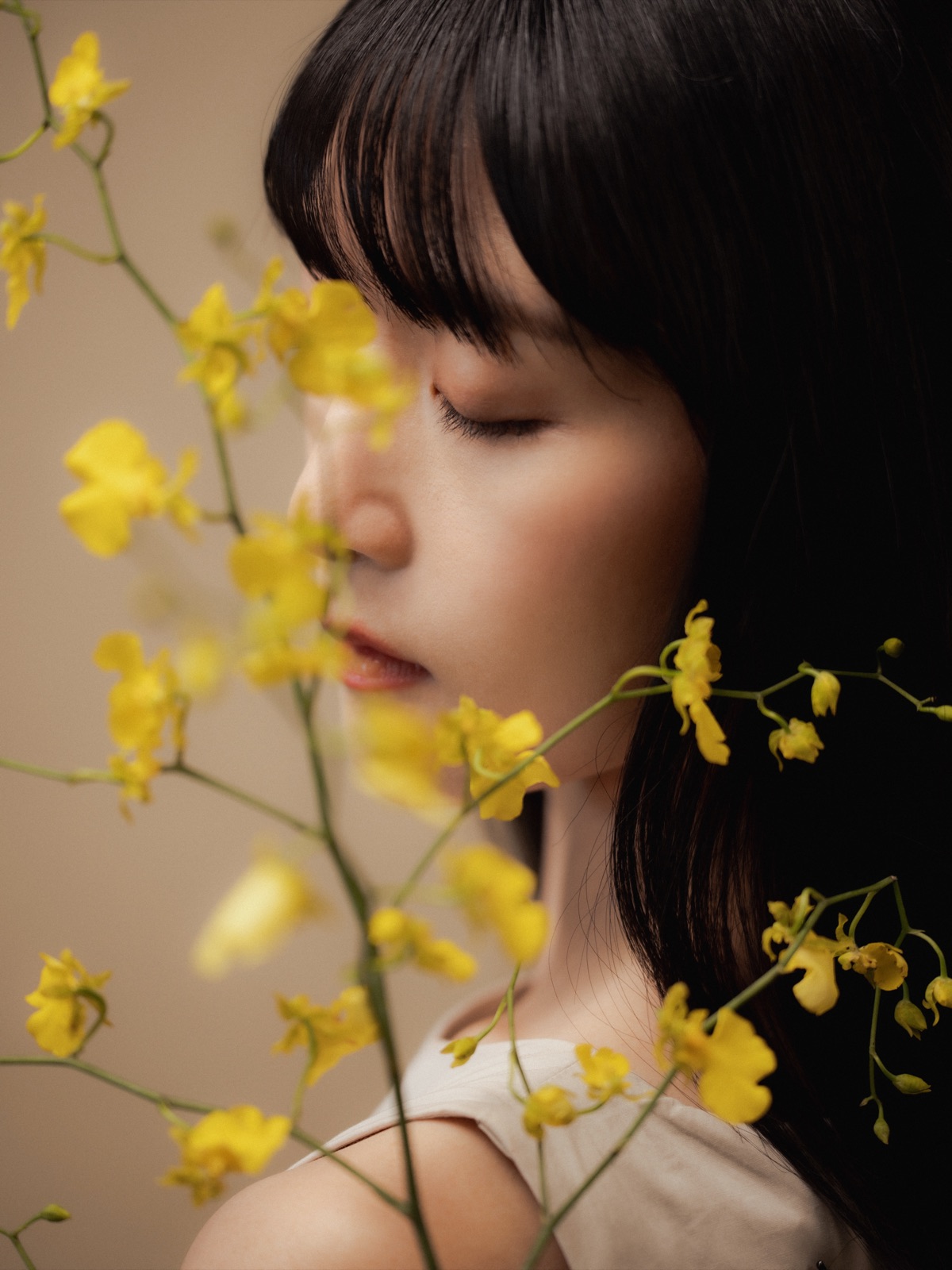 Model in soft profile behind sprays of yellow oncidium flowers, with natural, refined makeup